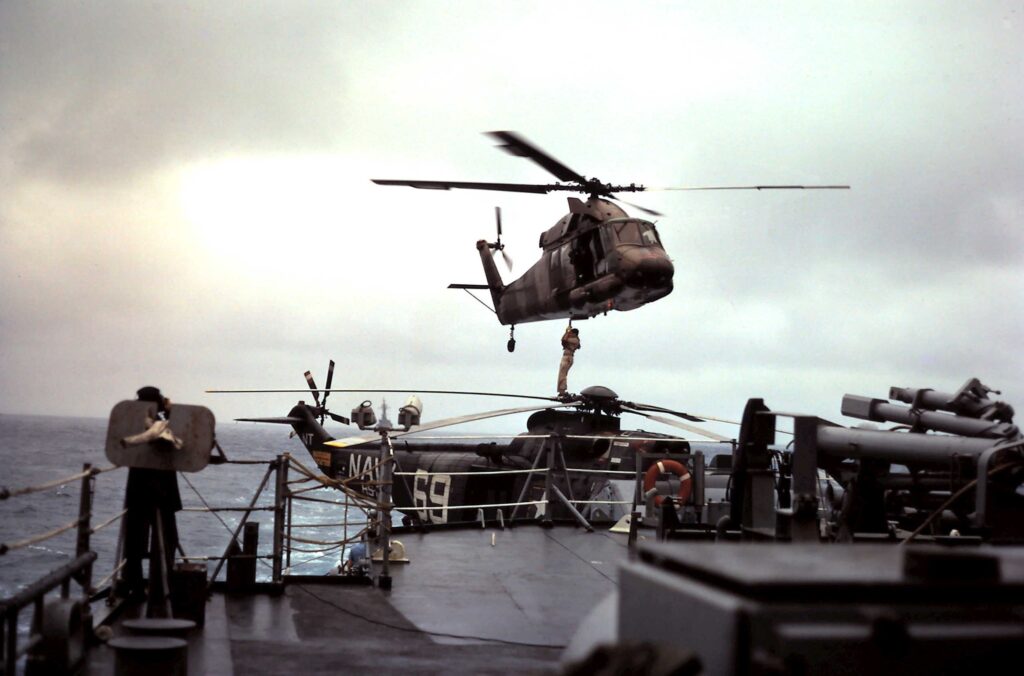 SAR operations in the Tonkin Gulf, Mar/Apr 1967 aboard the USS England (DLG 22). An SH-3 is parked on the fantail flight deck while a UH-2 picks up a traveler via sling. (NAVSOURCE)