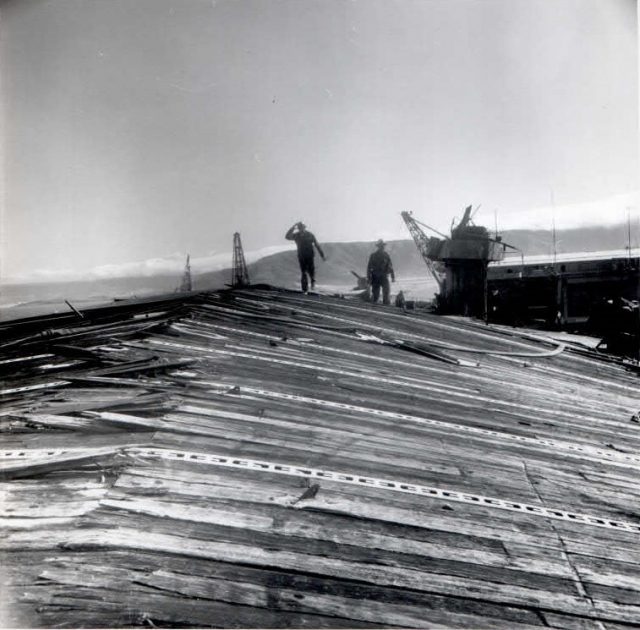 CVL-22 flight deck damage from the "Able" blast (as described above). The ships island and crane are behind and on the right side of the worker. (Photo:  Scan by John G. Lambert at NARA San Bruno, CA on the 2015 Independence mission.)